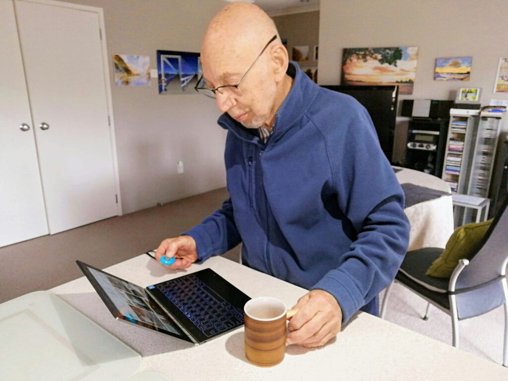 Een oudere man gebruikt een tablet aan de keukentafel, symbool voor de digitalisering en zelfstandigheid van senioren.