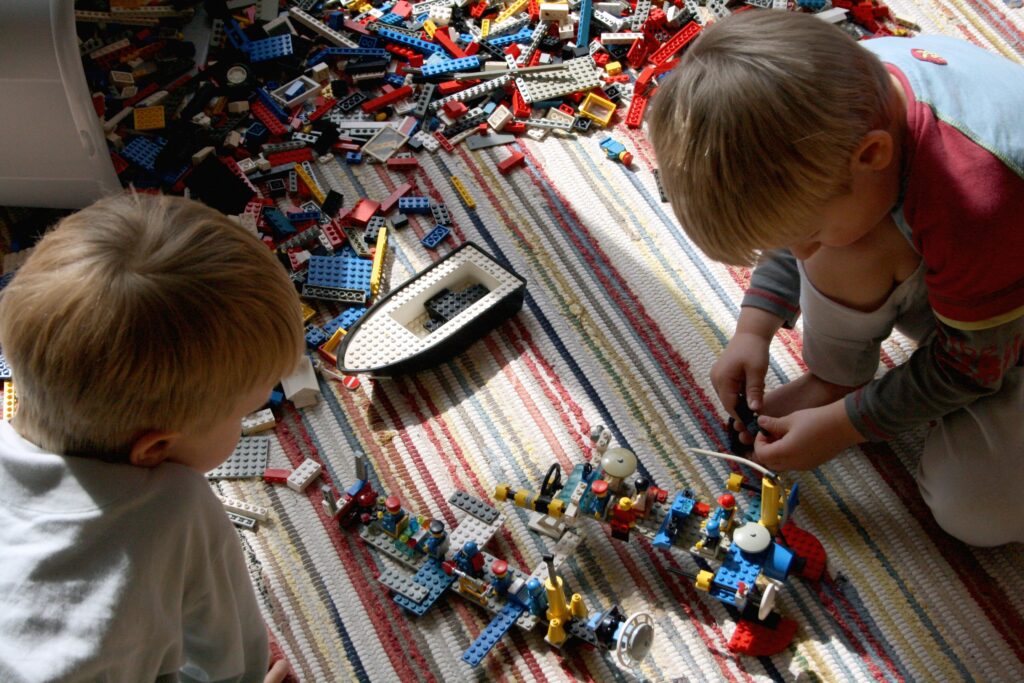 Twee kinderen bouwen met Lego op de vloer, symbool voor creativiteit en terugkeer naar de kern.