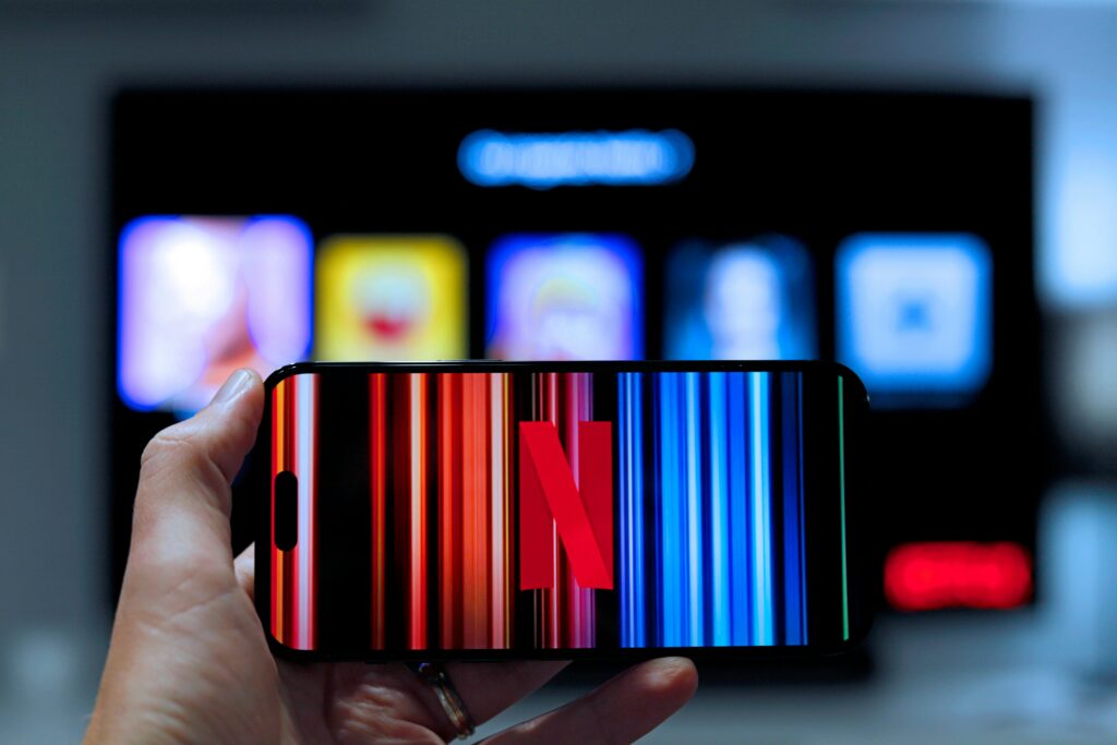 Een smartphone toont het Netflix-logo met op de achtergrond een tv-scherm, symbool voor het succes van abonnementsmodellen in entertainment.