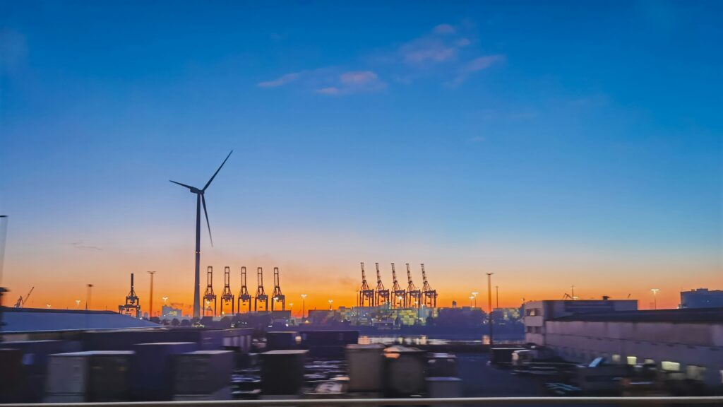 Een duurzame haven met kranen en een windturbine bij zonsondergang, symbool voor groene supply chains.