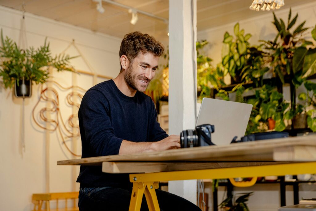 Een jonge ondernemer werkt glimlachend met een laptop in een lichte, groene werkruimte, symbool voor de toekomst van flexibel werken.