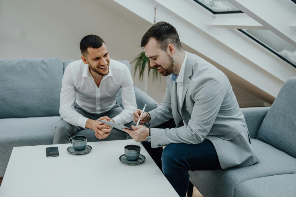 Twee ondernemers lachen en werken samen aan een deal, symbool voor het binnenhalen van de eerste klanten.